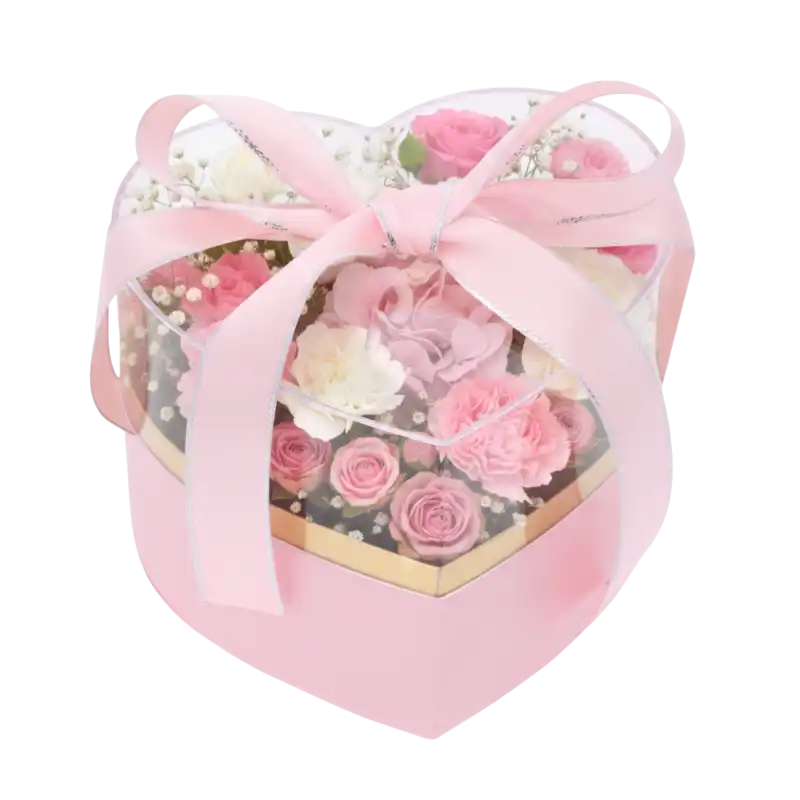 Różowy flower box w kształcie serca wypełniony kompozycją z różowych i białych róż oraz zielonych liści.
