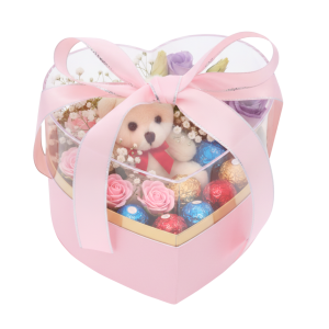 Flower box serce 15x14x12 cm z misiem, czekoladkami i kwiatami, zapakowany w przezroczyste pudełko z kokardą.