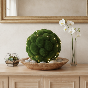 Kula z mchu umieszczona w drewnianej misie, opleciona subtelnymi światełkami LED, zestawiona z wazonem z orchideą i szklanym terrarium.