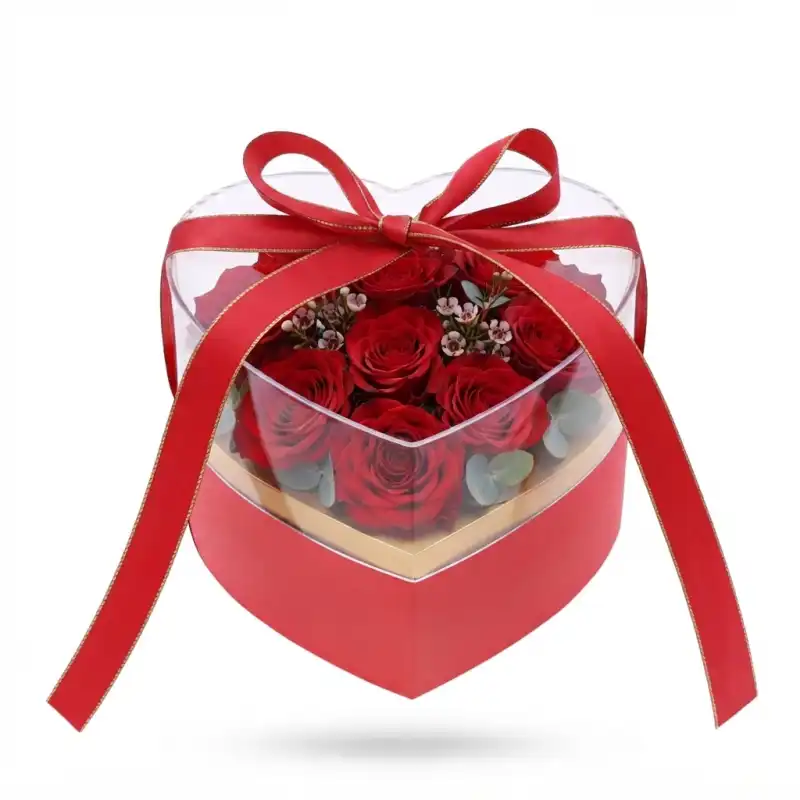 Czerwony flower box serce wypełniony różami, posiada przezroczystą pokrywkę i ozdobną wstążkę, idealny jako eleganckie artykuły dekoracyjne.
