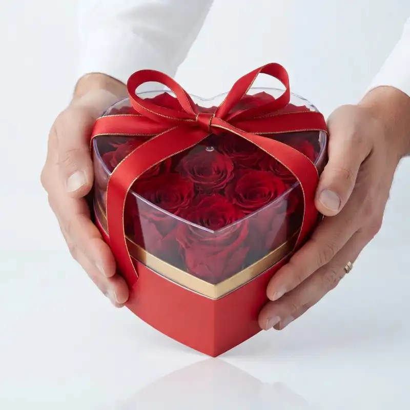 Męskie dłonie trzymające elegancki czerwony flower box w kształcie serca, pokazujący skalę pudełka i sposób jego prezentacji.