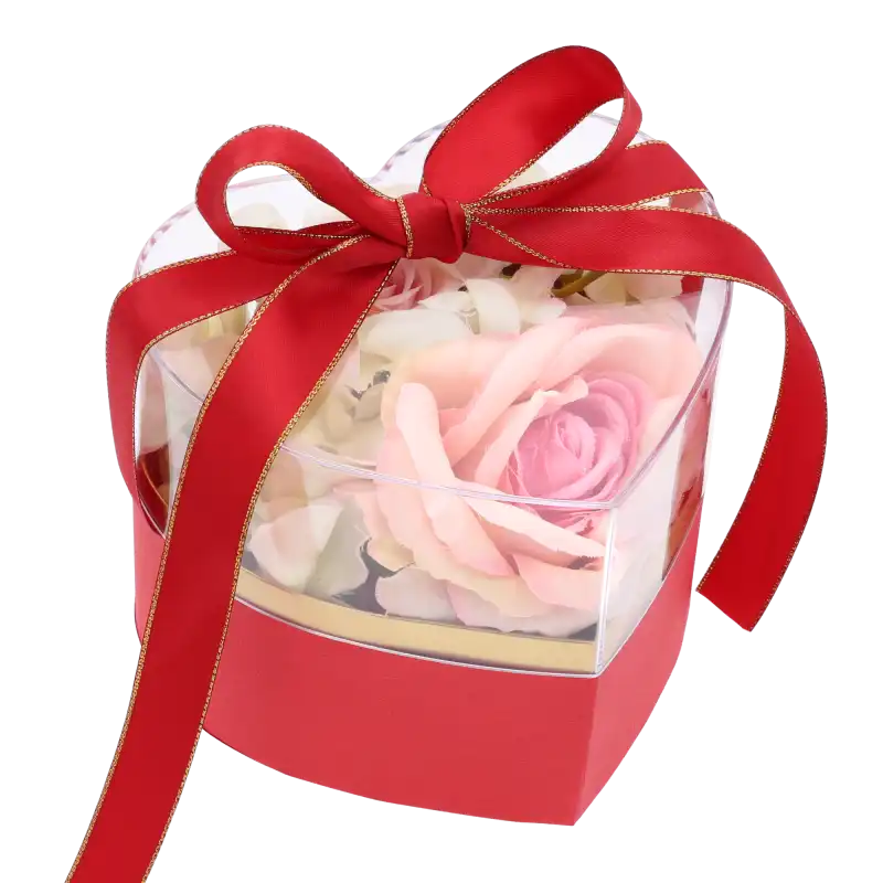Czerwony flower box z kompozycją kwiatową wewnątrz, zabezpieczony przezroczystą pokrywką z czerwoną kokardą.