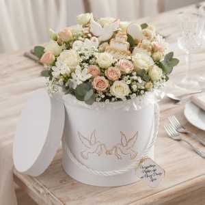 Dekoracyjny flower box 12 cm wypełniony bukietem róż i ślubnymi ciasteczkami w kształcie tortu i serc na stole.