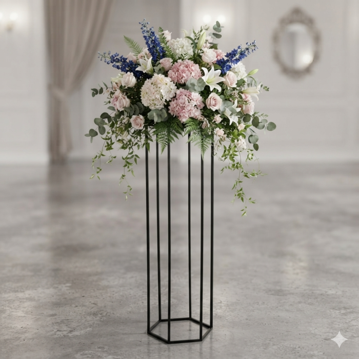Stojak heksagon w czarnym kolorze z bujną kompozycją kwiatową na szczycie. Wykonana z metalu konstrukcja stanowi elegancką podstawę dla roślin doniczkowych w jasnym wnętrzu.