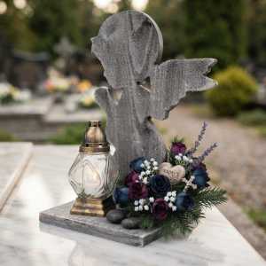 Statuetka nagrobna z aniołem w otoczeniu kompozycji kwiatowej i znicza, ukazująca gotowy stroik na cmentarz.