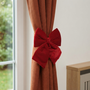 Czerwona welurowa kokarda 40 cm zamocowana jako elegancka ozdoba na brązowej zasłonie w jasnym wnętrzu.