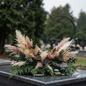 Czarne metalowe serce o szerokości 45 cm ustawione na nagrobku, wypełnione kompozycją z suszonych kwiatów, traw oraz delikatnych lampek LED.